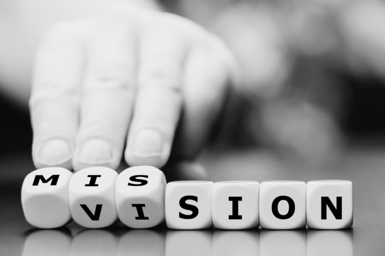 Une main au dessus de dés sur lesquels sont inscrits des lettres formant les mots vision et mission